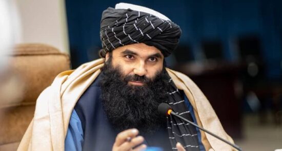 A man with a black and white turban speaks behind a news desk