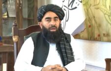 مردی با دستار سیاه و ریش بلند در اتاق با پرچم افغانستان