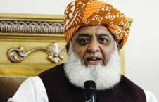 مرد مسن با دستار زردرنگ پشت میزک صحبت می‌کند