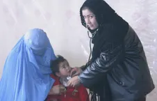کارمند صحی زن در حال معاینهٔ طفل با گوشی طبی در کنار زنی با چادری آبی