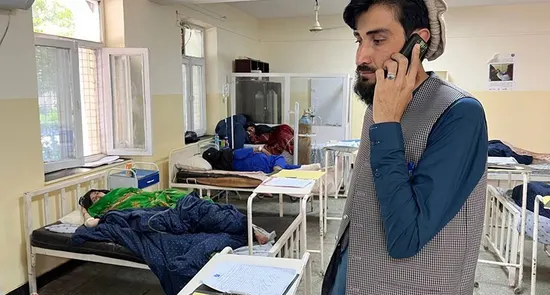 مردی در حال صحبت با تیلفون در دهلیز شفاخانه با مریضان بستری