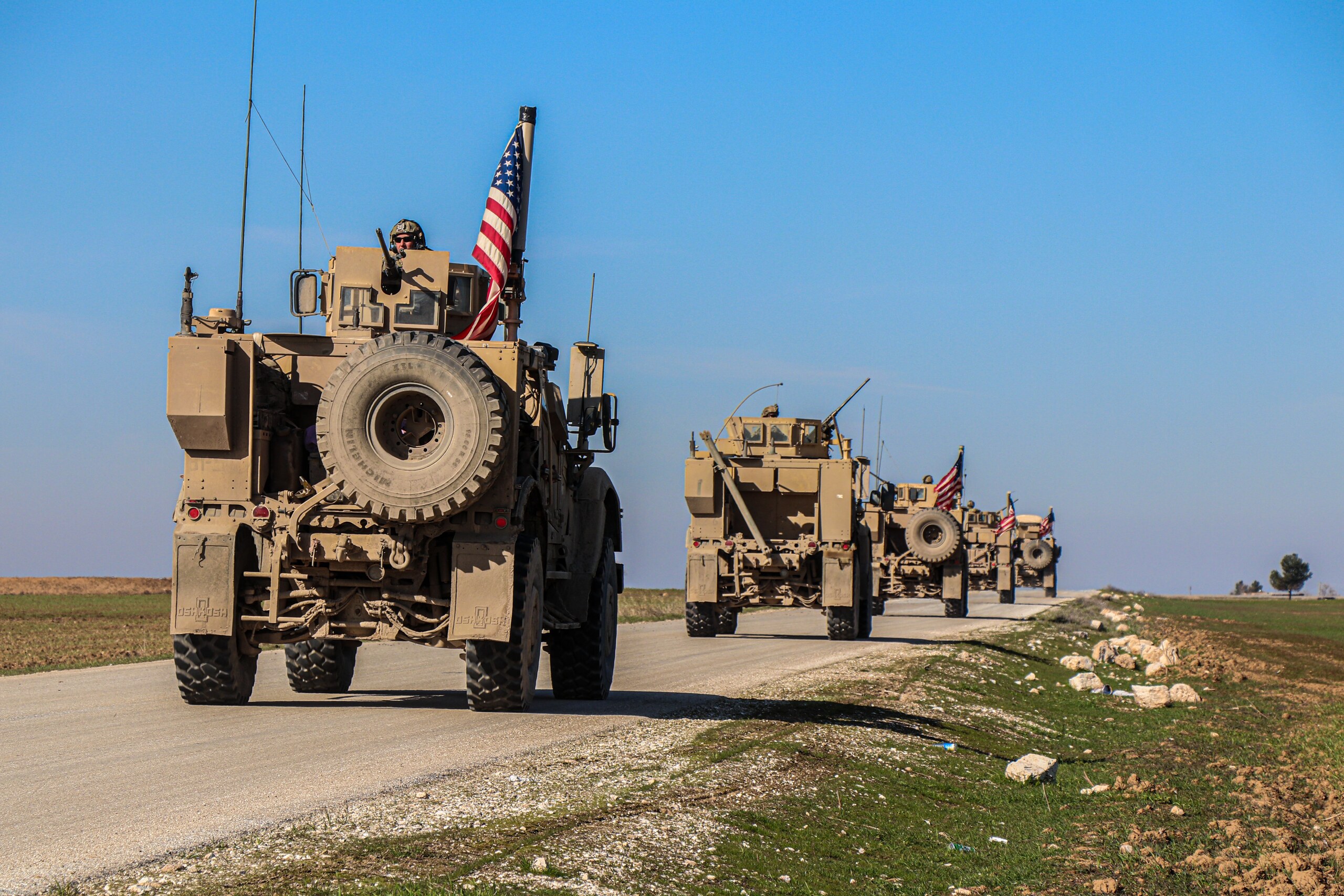 Military armored vehicles with an American flag on a rural road
