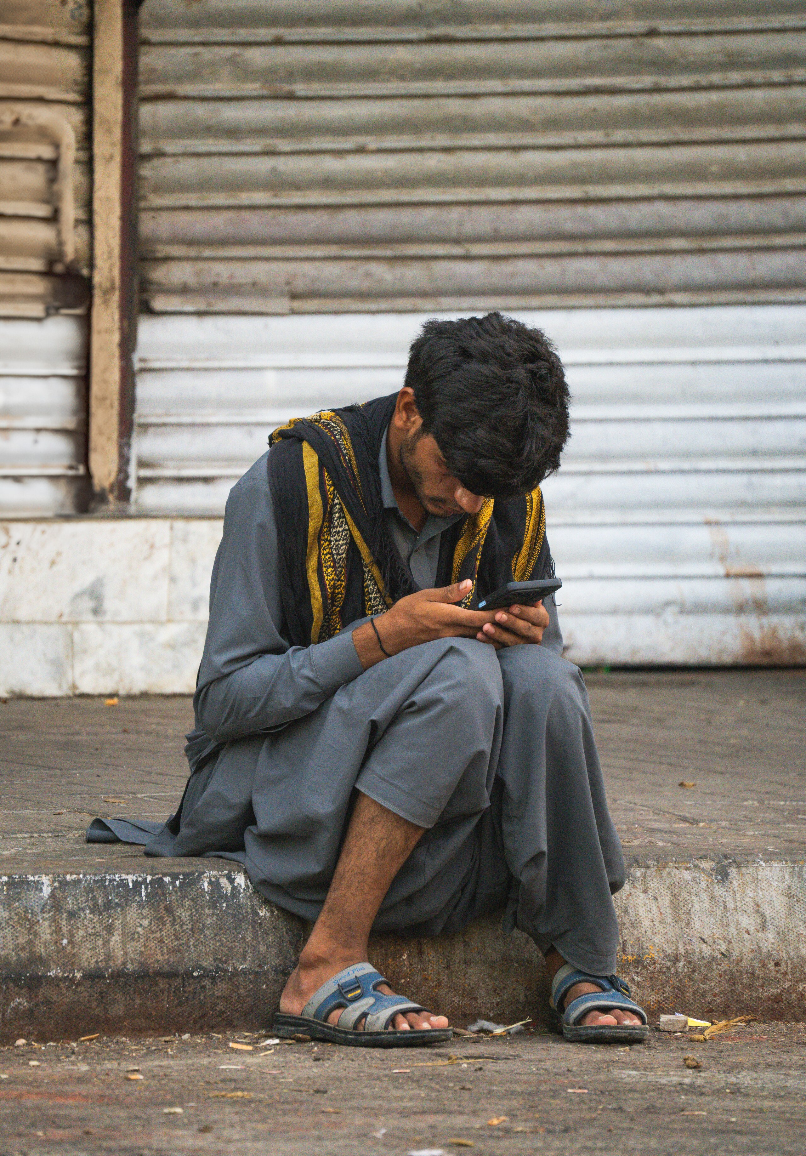 A young man sitting on the ground looking at a mobile phone